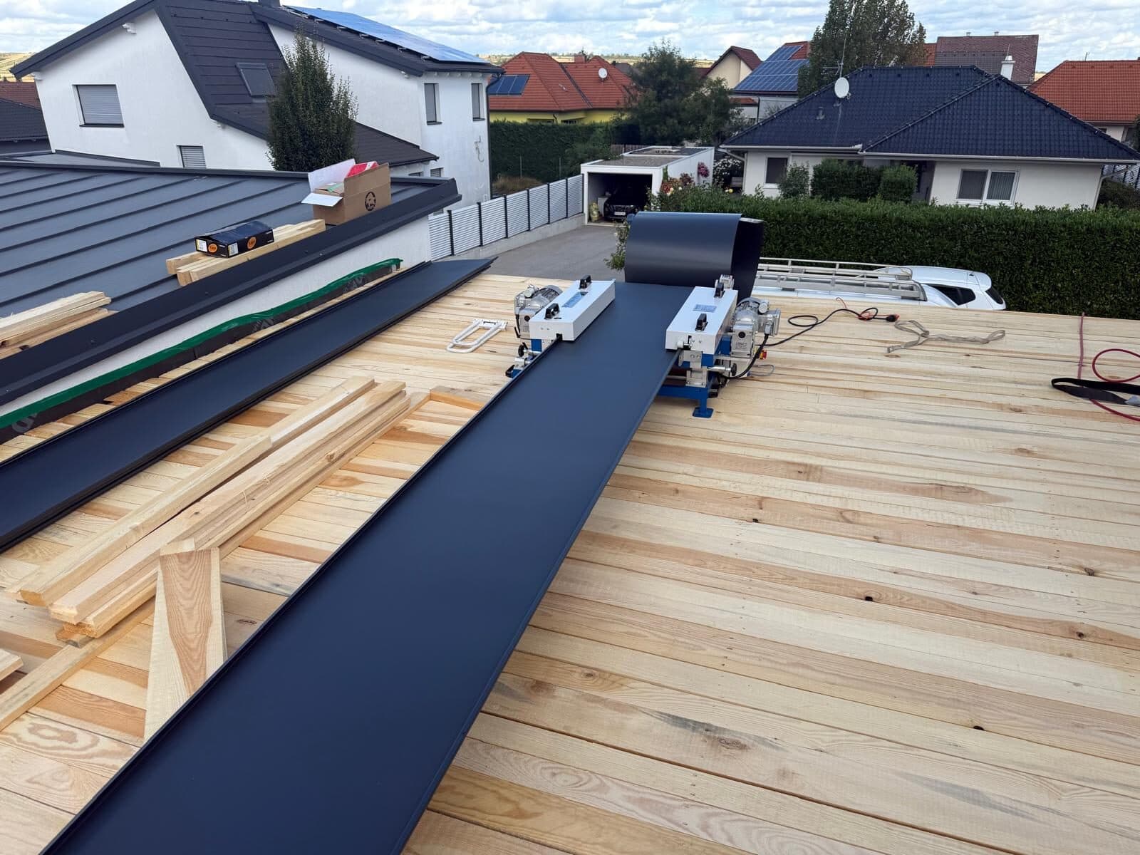 Frisch profilierte anthrazitfarbene Scharen liegen auf einer neuen Holzschalung neben der Profilieranlage.